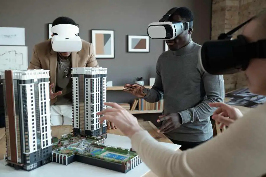 Group of architects in vr headsets standing around table with house layout during the presentation of new block of flats